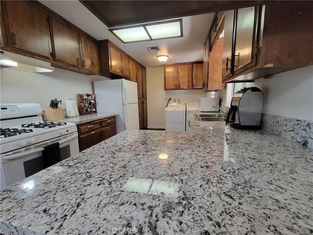 kitchen with sink, white appliances, kitchen peninsula, light stone countertops, and washer and dryer