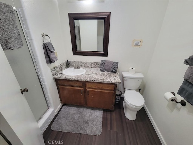 bathroom with toilet, a stall shower, vanity, wood finished floors, and baseboards