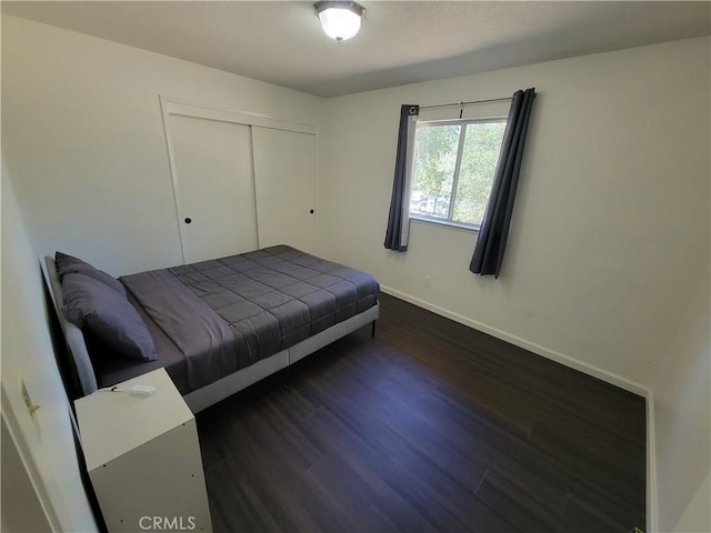 unfurnished bedroom with dark wood-type flooring, a closet, and baseboards