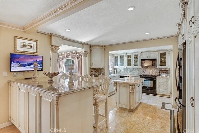 kitchen with a kitchen breakfast bar, black appliances, a center island, light stone counters, and decorative backsplash