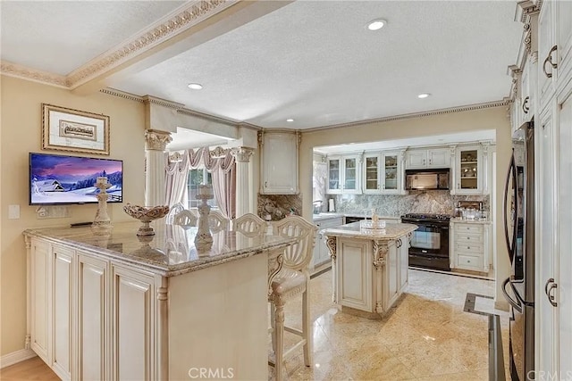 kitchen with a kitchen island, decorative backsplash, black appliances, crown molding, and light stone countertops