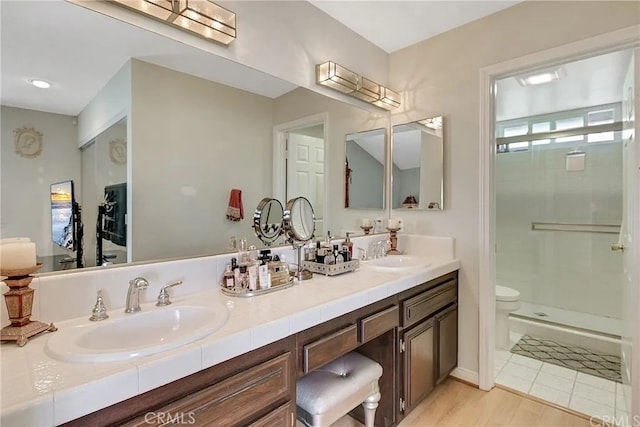 bathroom with toilet, a stall shower, double vanity, and a sink