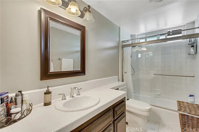 bathroom featuring a textured wall, bath / shower combo with glass door, vanity, and toilet