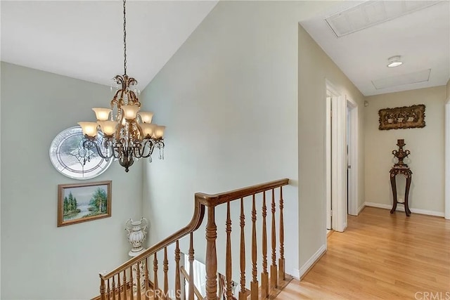 hall with baseboards, lofted ceiling, an inviting chandelier, an upstairs landing, and light wood-style floors