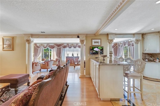 kitchen featuring light stone countertops, a textured ceiling, light hardwood / wood-style floors, ornate columns, and a breakfast bar area