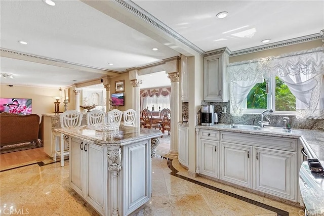 kitchen featuring a kitchen island, open floor plan, a sink, ornate columns, and backsplash