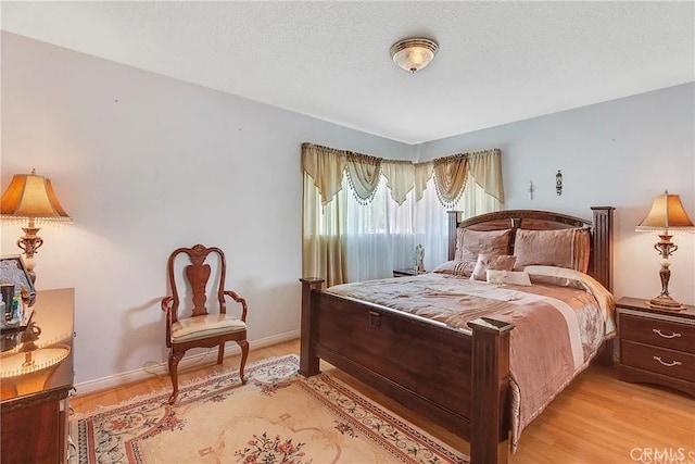 bedroom featuring light wood-type flooring, baseboards, and a textured ceiling