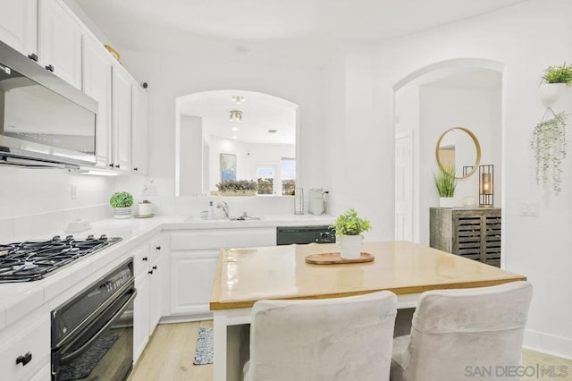 kitchen with black appliances, a breakfast bar, a kitchen island, sink, and white cabinetry