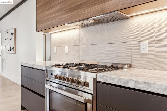 kitchen with light stone counters, light wood-type flooring, wall chimney range hood, and gas range