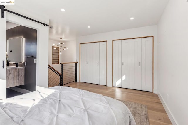 bedroom featuring an inviting chandelier, two closets, a barn door, and light hardwood / wood-style flooring