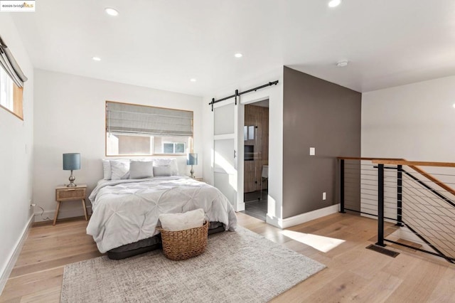 bedroom with a barn door, light hardwood / wood-style flooring, and connected bathroom