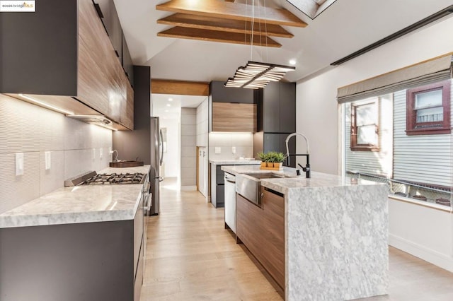 kitchen with a center island with sink, tasteful backsplash, light wood-type flooring, appliances with stainless steel finishes, and sink