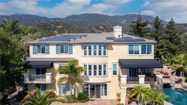 rear view of property with a balcony, a mountain view, and solar panels