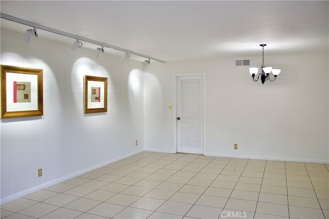 tiled empty room featuring track lighting and an inviting chandelier