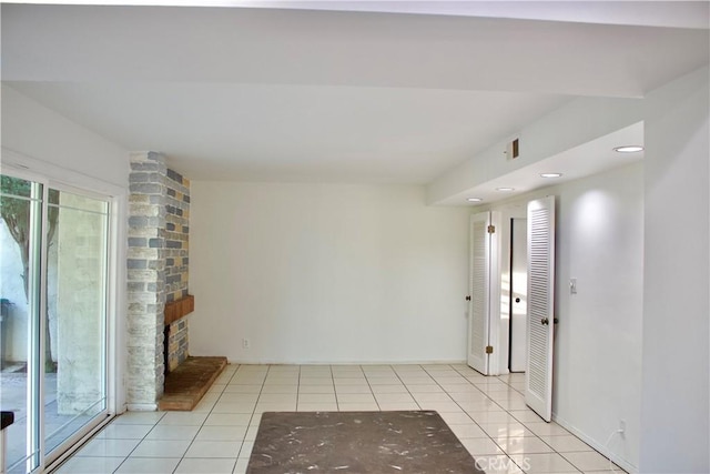 unfurnished room with a stone fireplace, light tile patterned flooring, and plenty of natural light