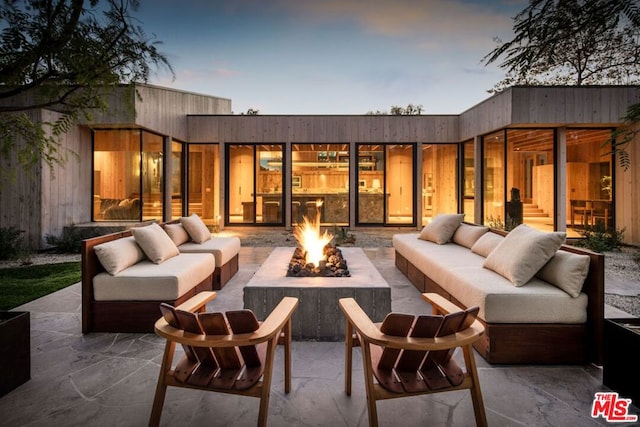 back house at dusk with a patio area and an outdoor living space with a fire pit