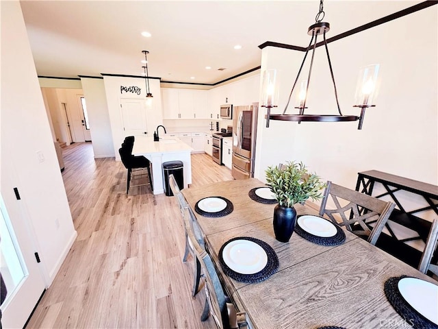 dining space with sink, ornamental molding, light wood-type flooring, and a notable chandelier