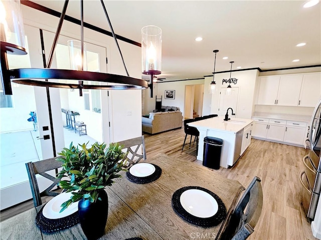 kitchen with a center island with sink, light wood-type flooring, pendant lighting, white cabinets, and sink