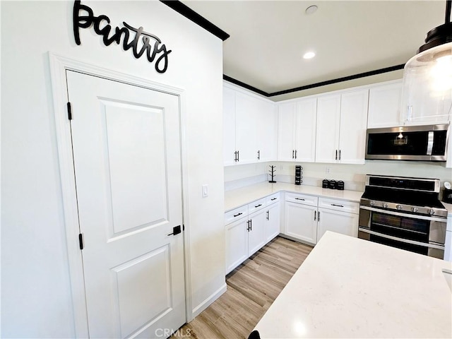 kitchen featuring stainless steel appliances, light hardwood / wood-style floors, white cabinets, and hanging light fixtures