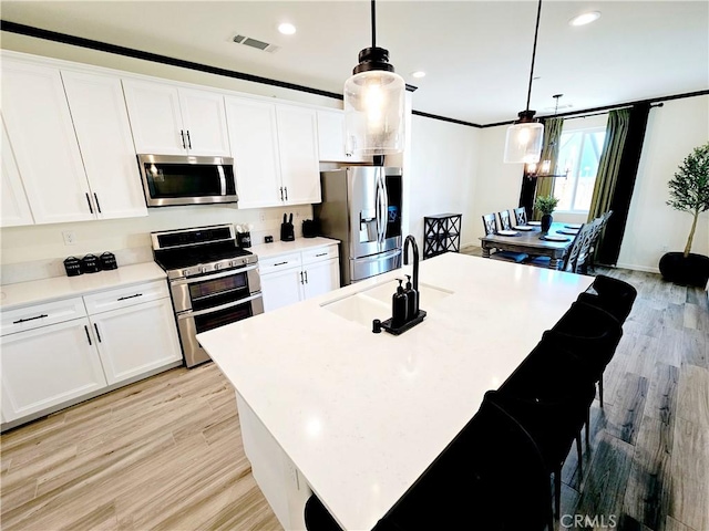 kitchen featuring decorative light fixtures, white cabinets, a center island with sink, and appliances with stainless steel finishes