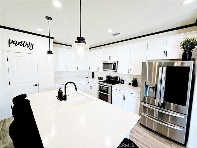 kitchen featuring appliances with stainless steel finishes, hanging light fixtures, light hardwood / wood-style floors, white cabinets, and sink