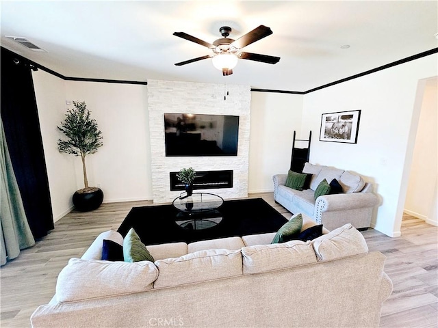 living room featuring light hardwood / wood-style floors, ceiling fan, a stone fireplace, and ornamental molding