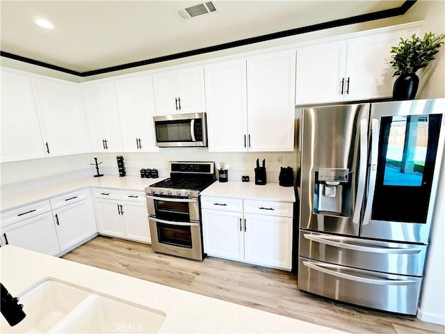 kitchen featuring stainless steel appliances, white cabinets, decorative backsplash, and light wood-type flooring