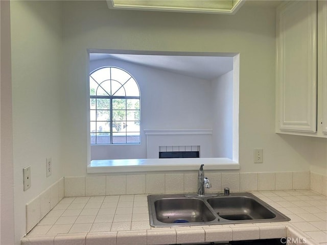 kitchen featuring tile countertops, a fireplace, a sink, and white cabinets