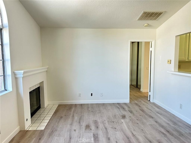 unfurnished living room featuring light wood finished floors, visible vents, baseboards, a tile fireplace, and a textured ceiling