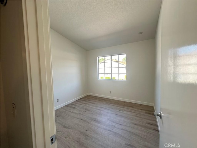 spare room featuring a textured ceiling, baseboards, lofted ceiling, and light wood-style floors