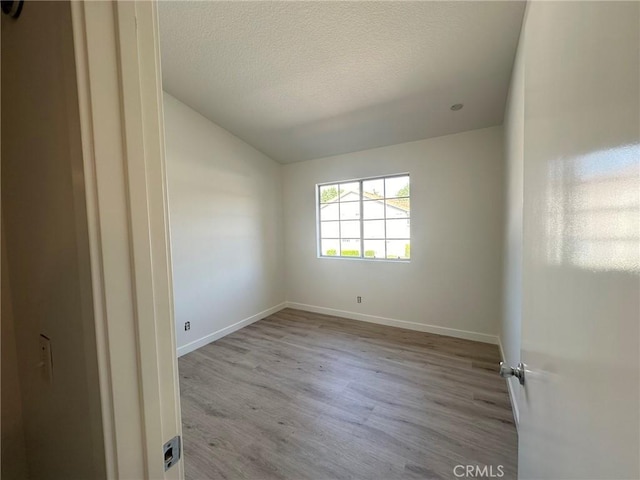 unfurnished room featuring vaulted ceiling, wood finished floors, baseboards, and a textured ceiling