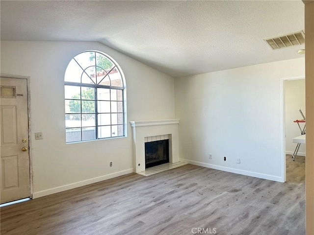 unfurnished living room with visible vents, a textured ceiling, wood finished floors, lofted ceiling, and a tile fireplace