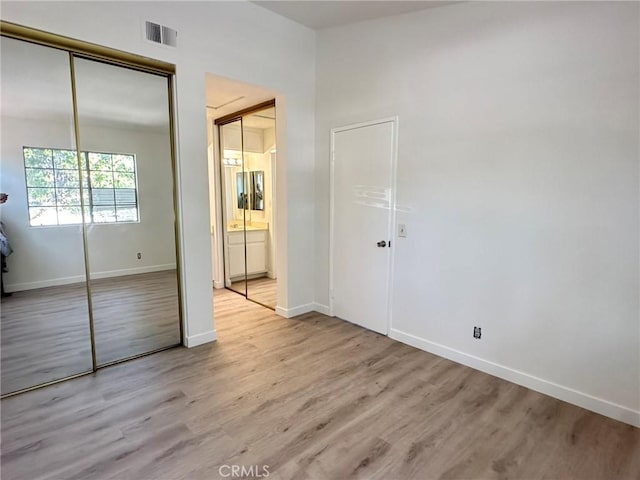 unfurnished bedroom with light wood-type flooring, baseboards, visible vents, and connected bathroom