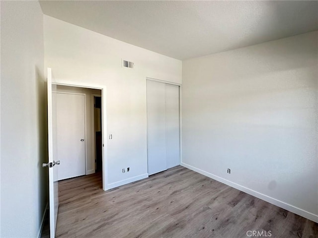 unfurnished bedroom featuring a closet, visible vents, baseboards, and wood finished floors