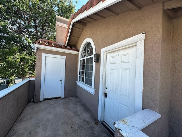 property entrance featuring a tiled roof, a balcony, and stucco siding