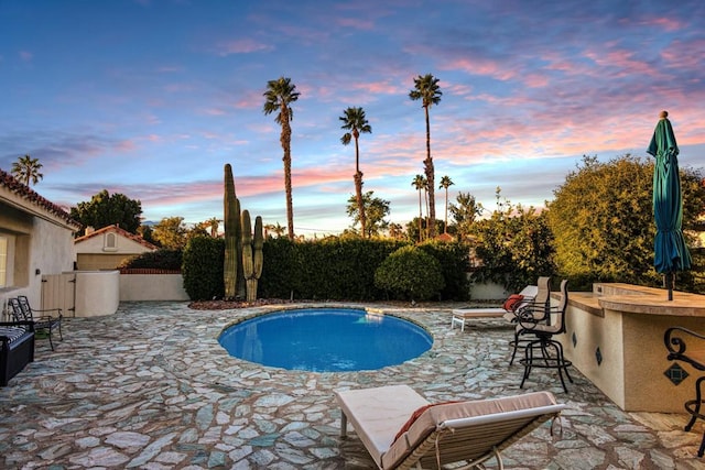 pool at dusk featuring an outdoor bar and a patio