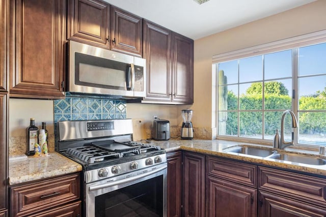 kitchen with light stone counters, stainless steel appliances, dark brown cabinetry, and sink