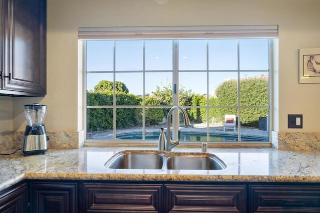 kitchen featuring sink, dark brown cabinets, and light stone countertops