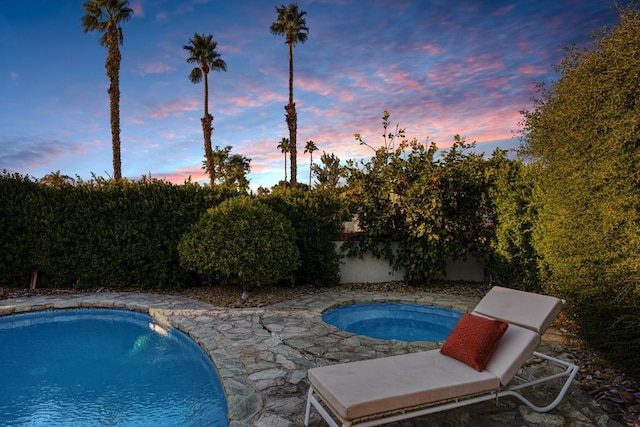 pool at dusk with an in ground hot tub