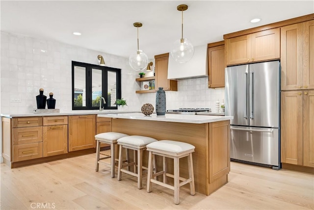 kitchen with light hardwood / wood-style flooring, a kitchen island, backsplash, high end fridge, and a kitchen breakfast bar