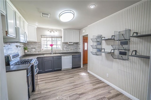 kitchen with white appliances, light hardwood / wood-style floors, backsplash, white cabinets, and sink