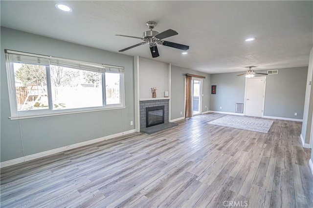 unfurnished living room featuring ceiling fan, light wood-type flooring, and a brick fireplace