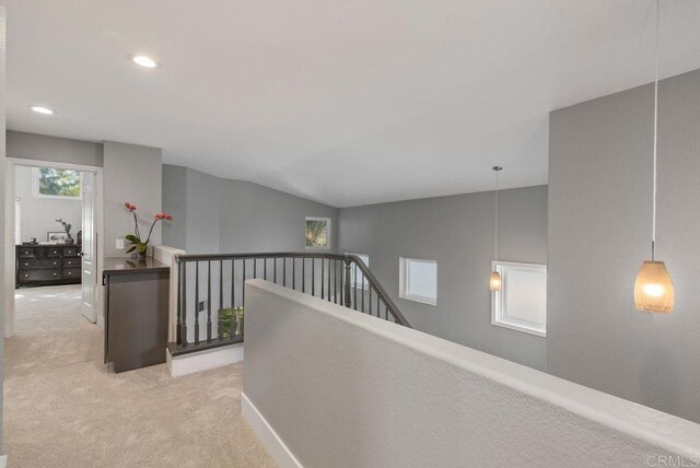 corridor featuring lofted ceiling, plenty of natural light, and light colored carpet