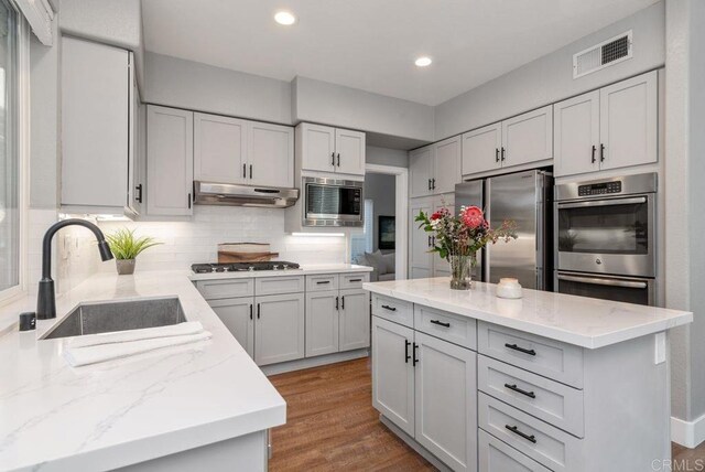 kitchen with light stone counters, tasteful backsplash, a kitchen island, appliances with stainless steel finishes, and sink