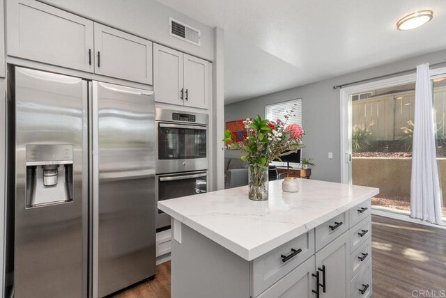 kitchen with stainless steel appliances, white cabinetry, light stone countertops, dark hardwood / wood-style floors, and a kitchen island