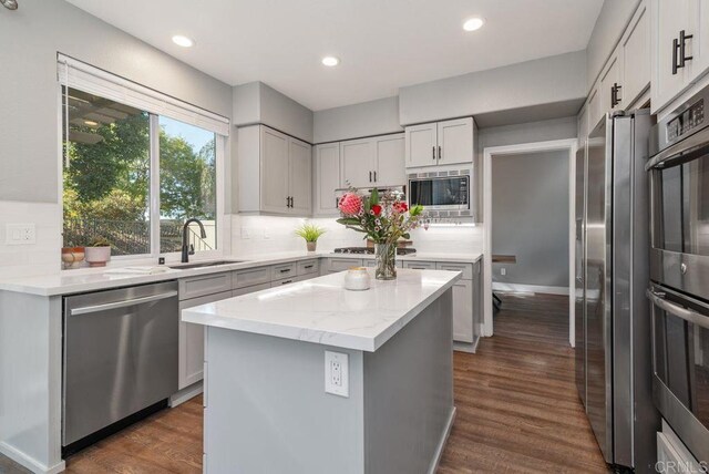 kitchen featuring appliances with stainless steel finishes, light stone countertops, dark hardwood / wood-style floors, a kitchen island, and sink