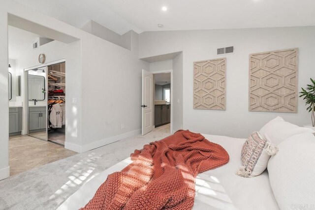 carpeted bedroom with ensuite bath, a spacious closet, a closet, lofted ceiling, and sink