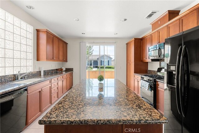 kitchen with light tile patterned floors, black appliances, a kitchen island, and dark stone countertops