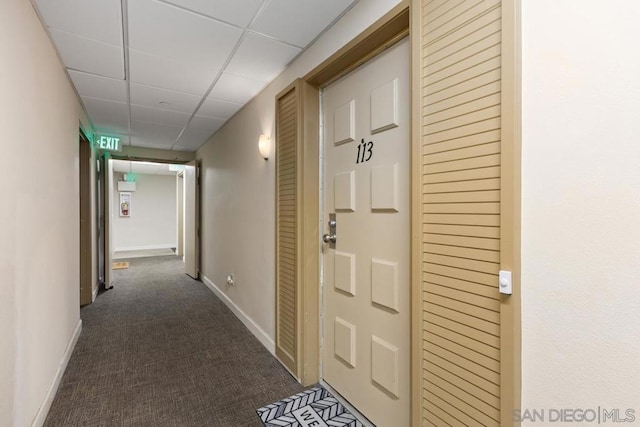 hall featuring dark carpet and a paneled ceiling