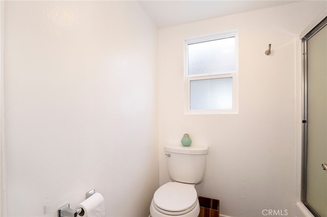 bathroom featuring toilet and a shower with shower door